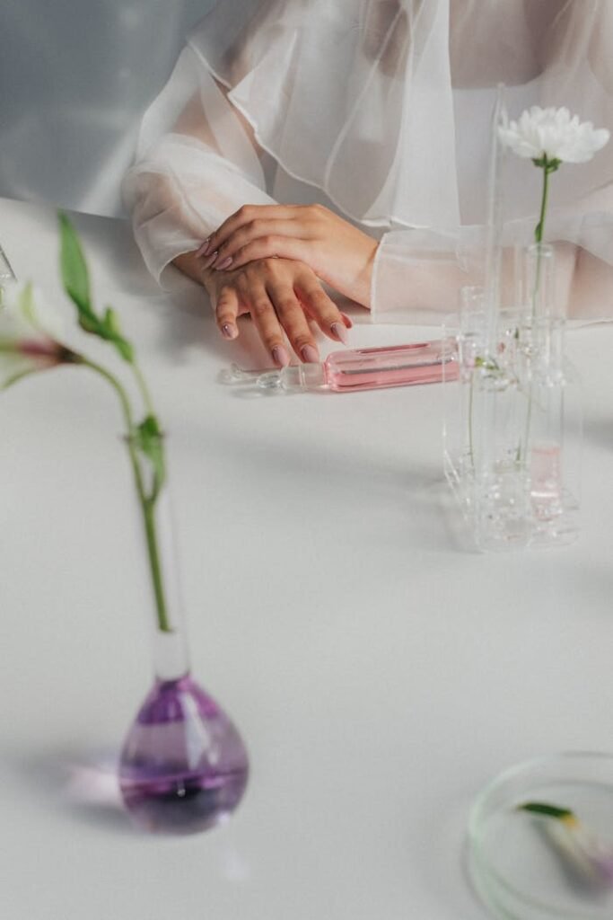 Elegant hands resting on a table with laboratory glassware and flowers, conveying a scientific botanical theme.