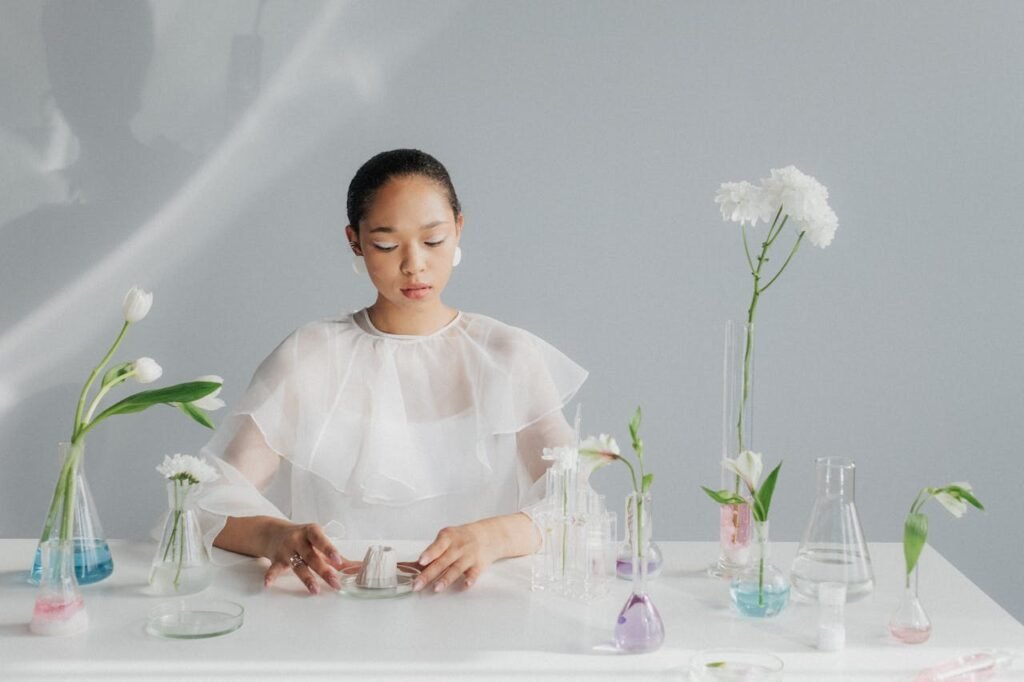 A woman in a sheer white outfit conducting a floral-themed laboratory experiment, blending art and science.